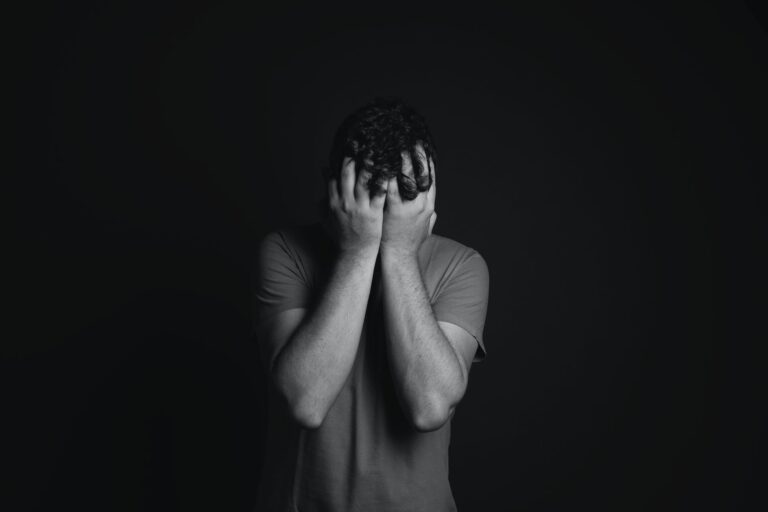 depressed man with face in his hands; black background